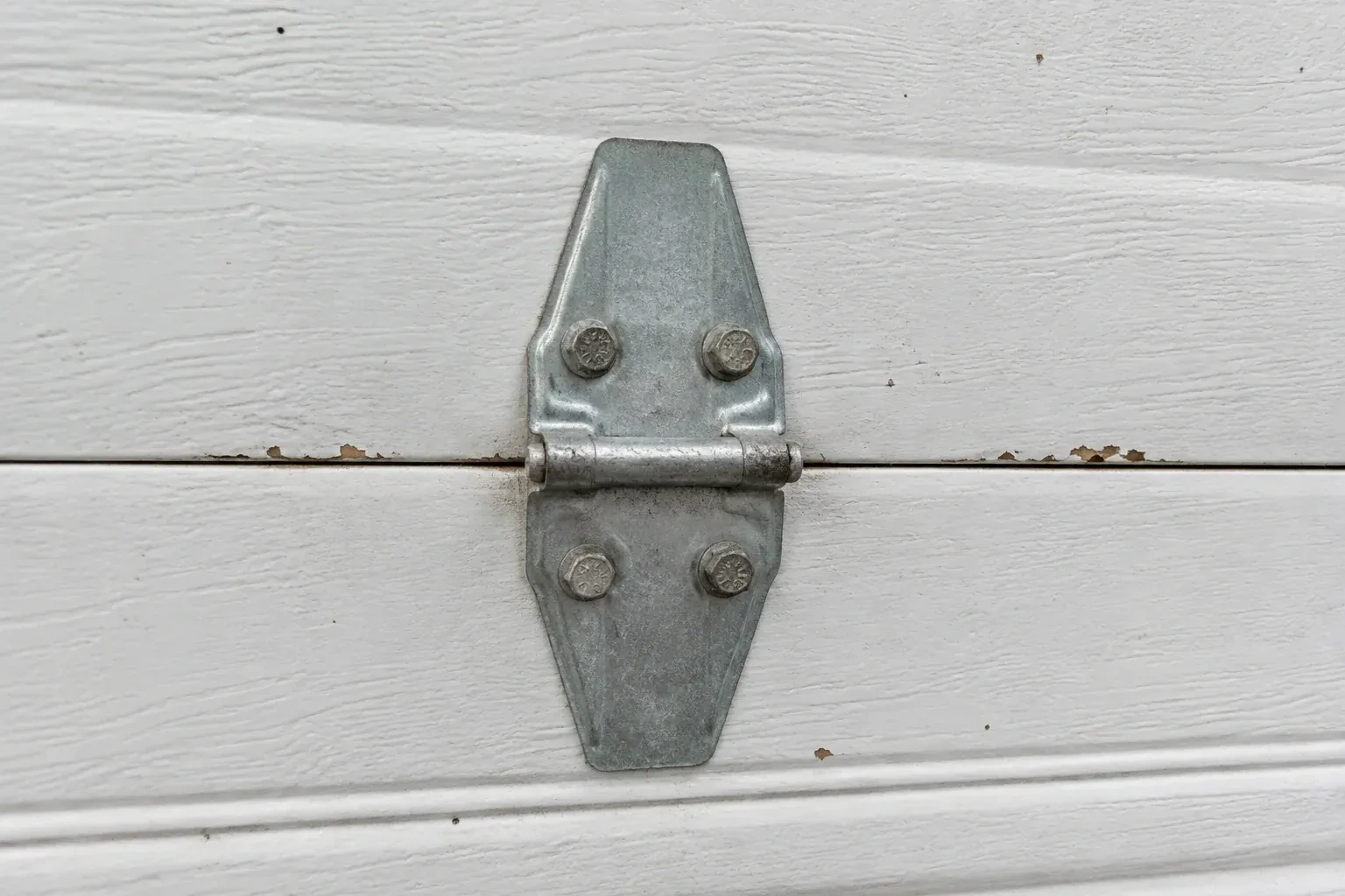 Metal center hinge across a seam in a white sectional garage door. — Garage Door Hinge Replacement, Burlington
