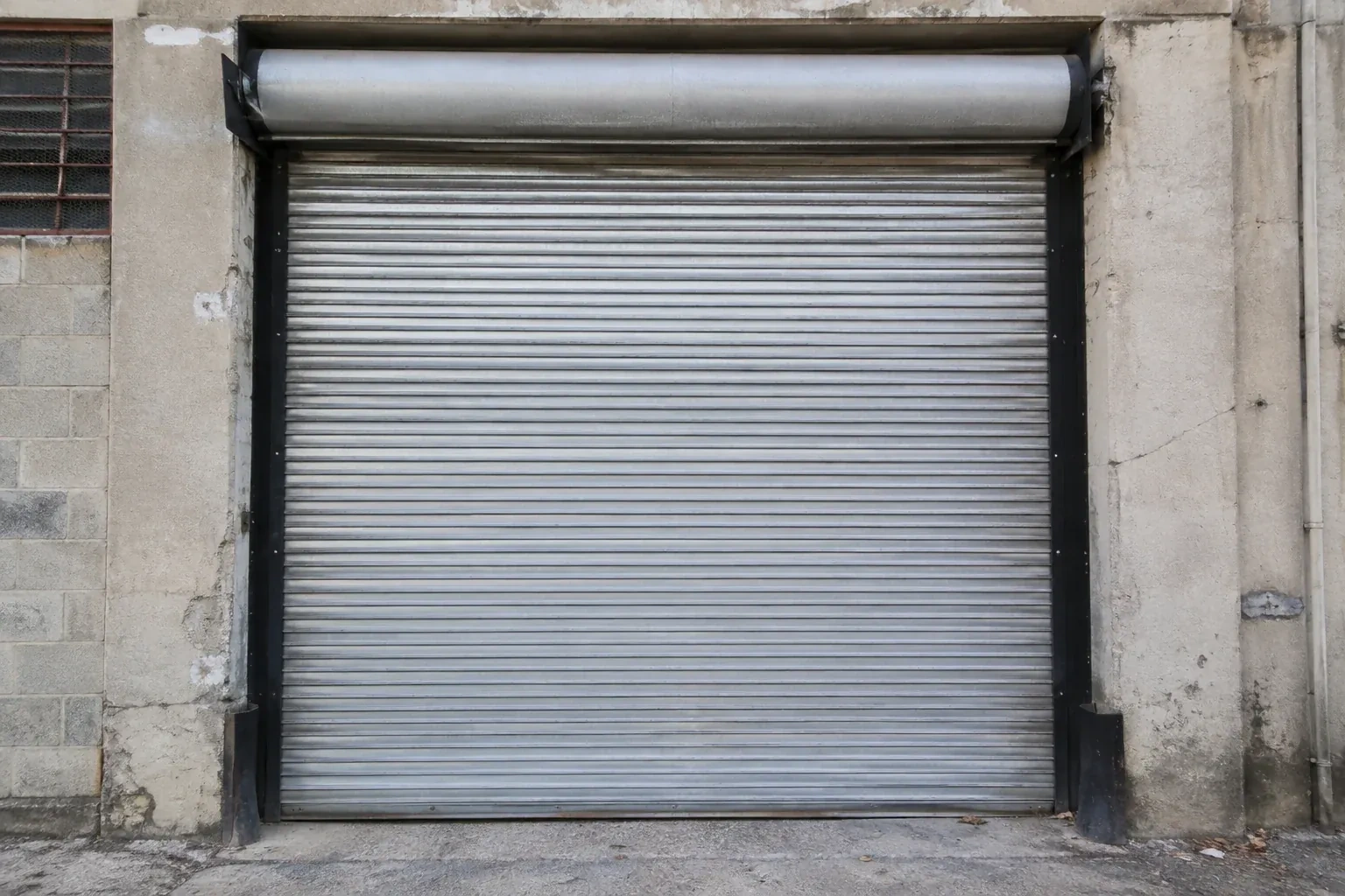 Closed metal rolling shutter in a weathered warehouse opening. — Commercial Rolling Door Repair, Burlington