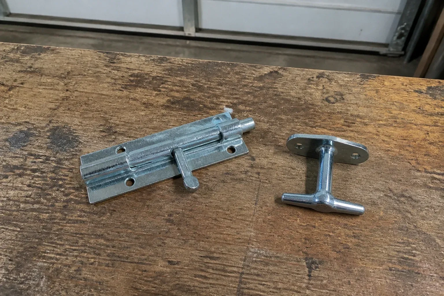 Detached slide bolt and T-handle on a wooden garage workbench. — Garage Door Manual Lock Repair, Burlington