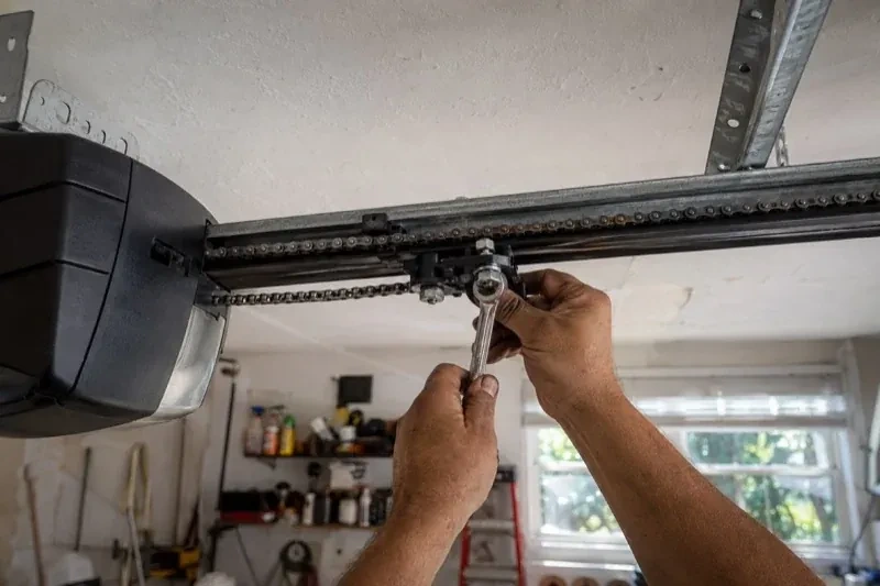 Hands holding a wrench against an opener trolley beneath a chain rail — Chain-Drive Opener Repair, Burlington