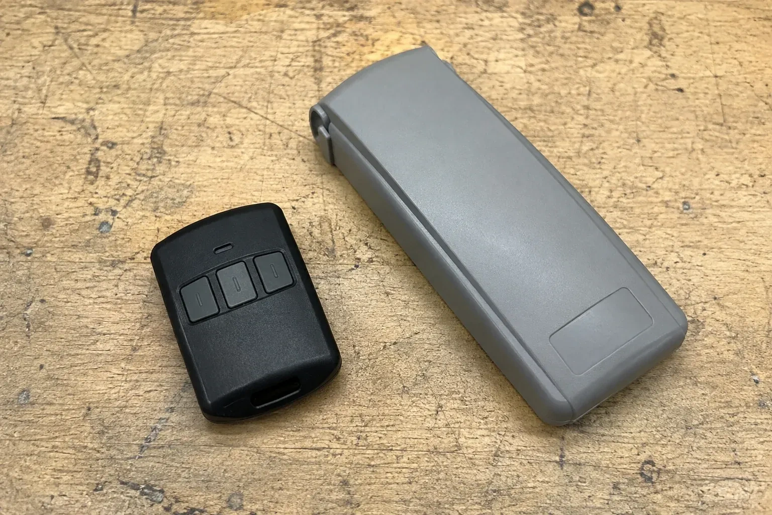 Three-button remote beside a closed grey keypad cover on a workbench. — Garage Door Remote and Keypad Programming, Burlington