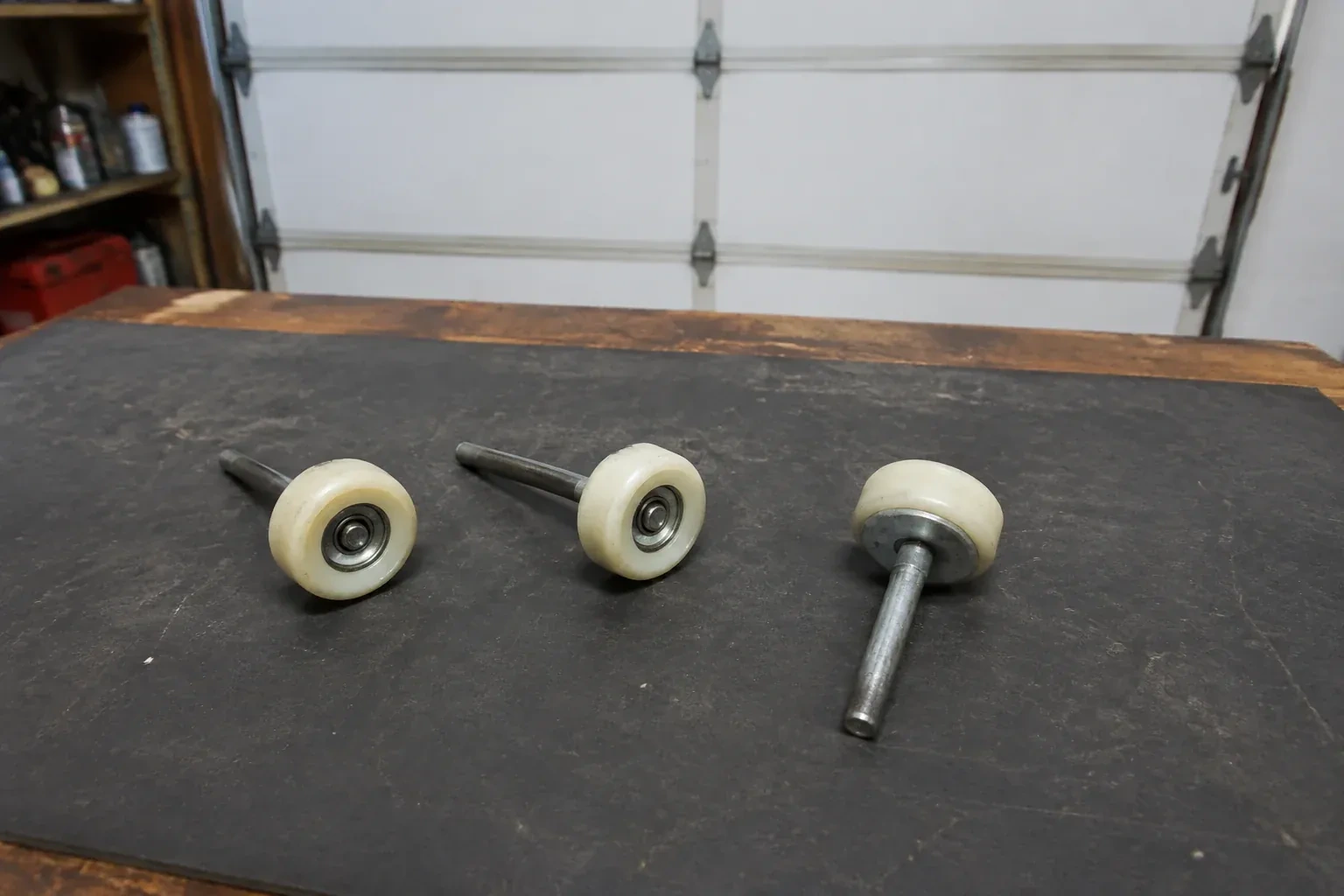 Three detached nylon-wheel garage door rollers with steel stems on a work mat. — Garage Door Roller Replacement, Burlington